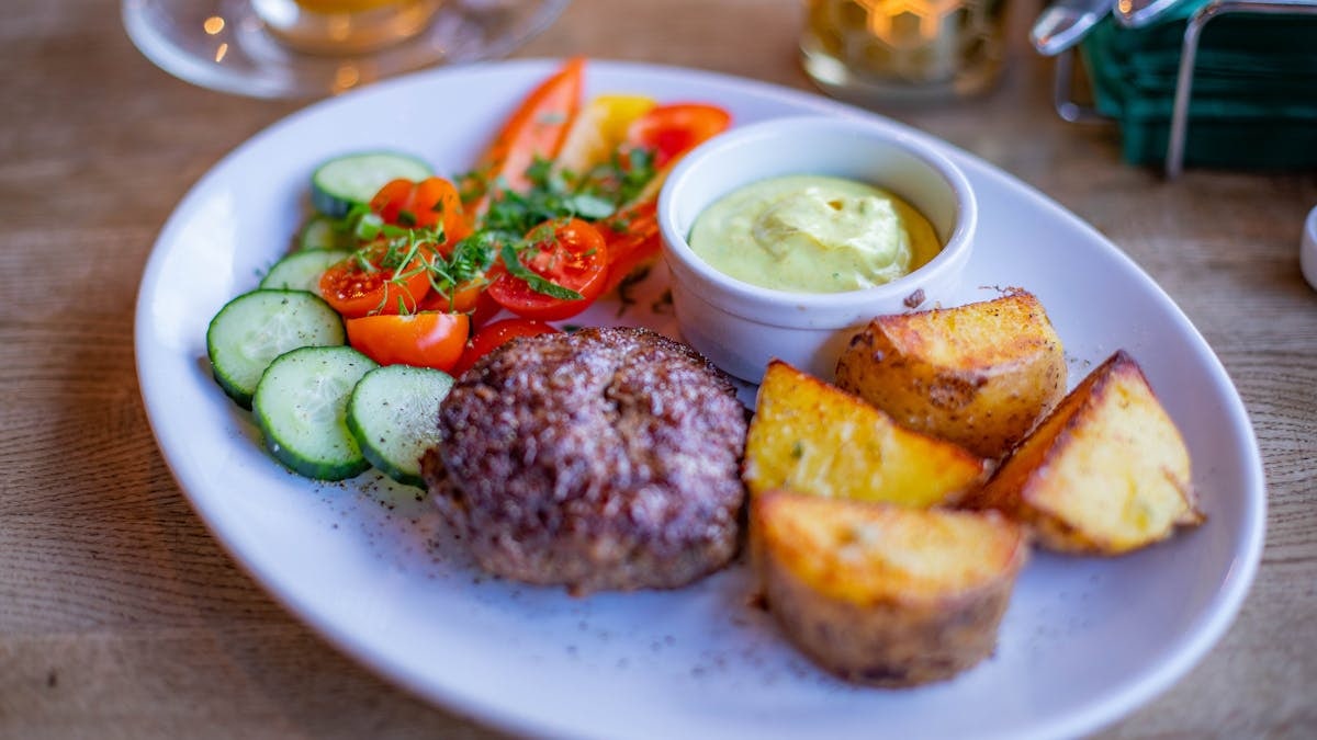 A well-presented gourmet meal featuring grilled patty, potatoes, and fresh vegetables.